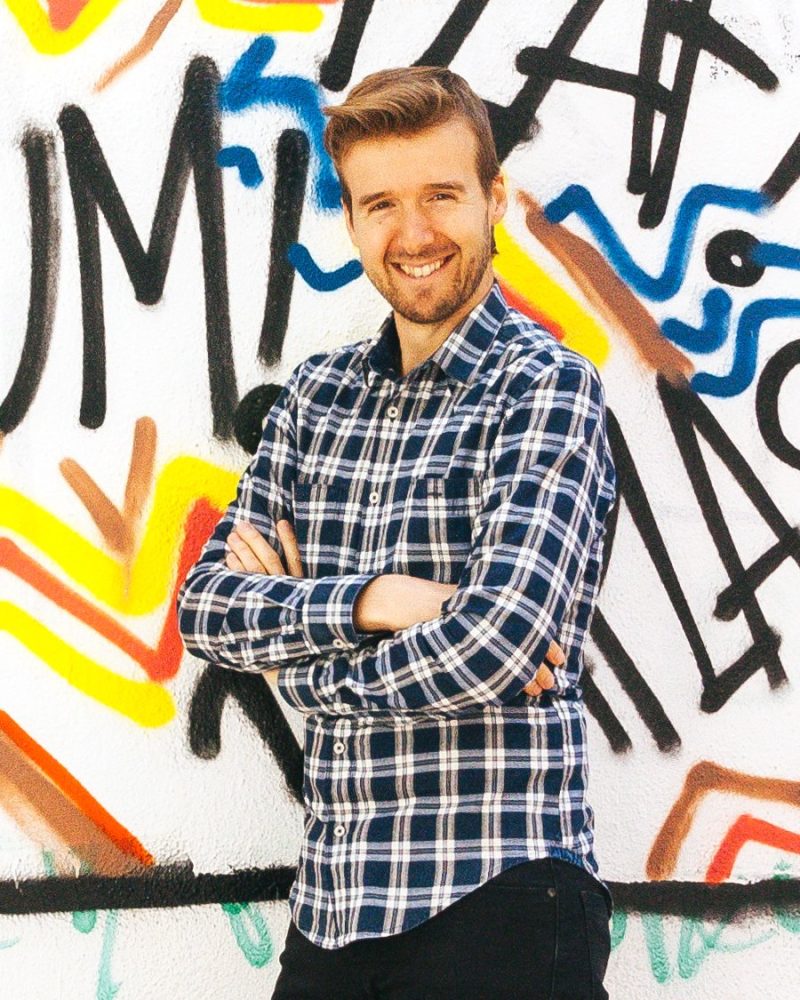 Javier Mir sonriendo, con los brazos cruzados, delante de una pared con grafitis